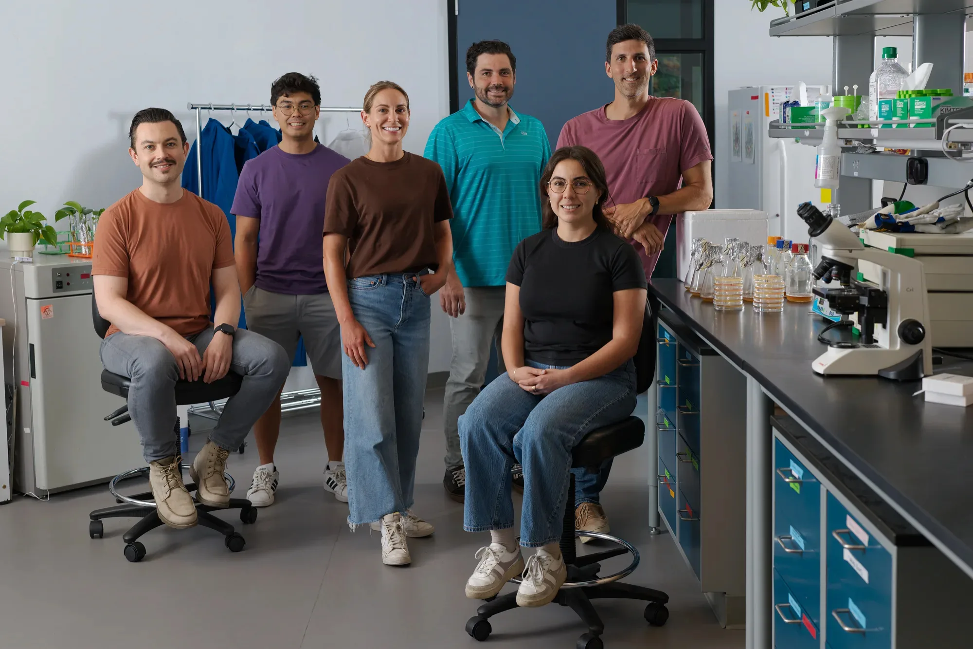 Six members of the Nurture team in the lab, beside a bench with culture flasks and a microscope.